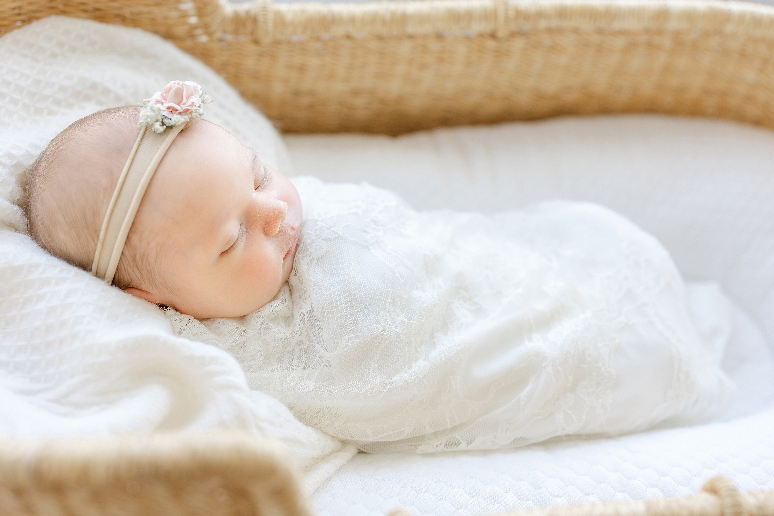 A newborn baby girl wrapped in a lace swaddle in a billy basket.