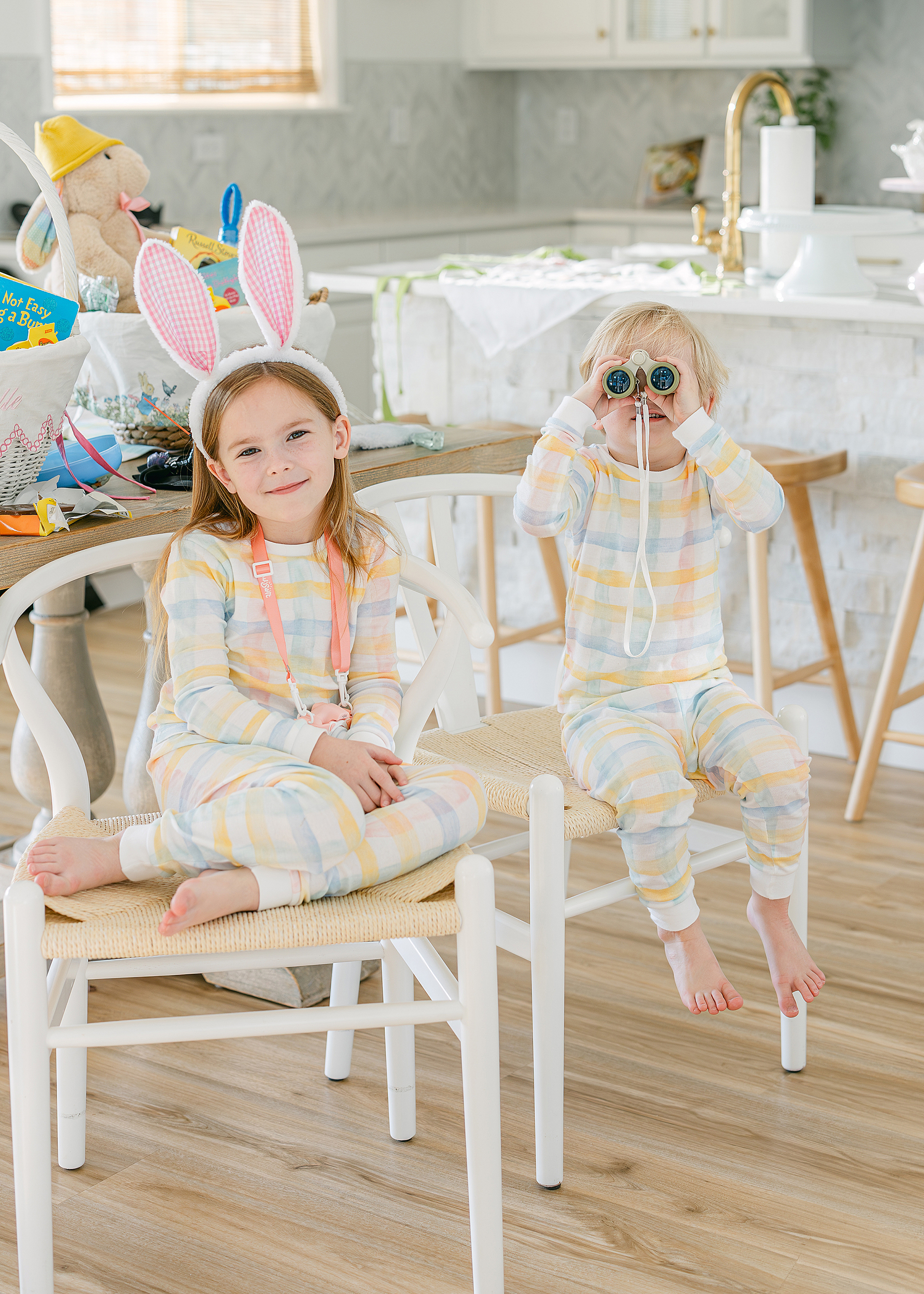 Two little children sit together on Easter wearing pastel pajamas in their kitchen.