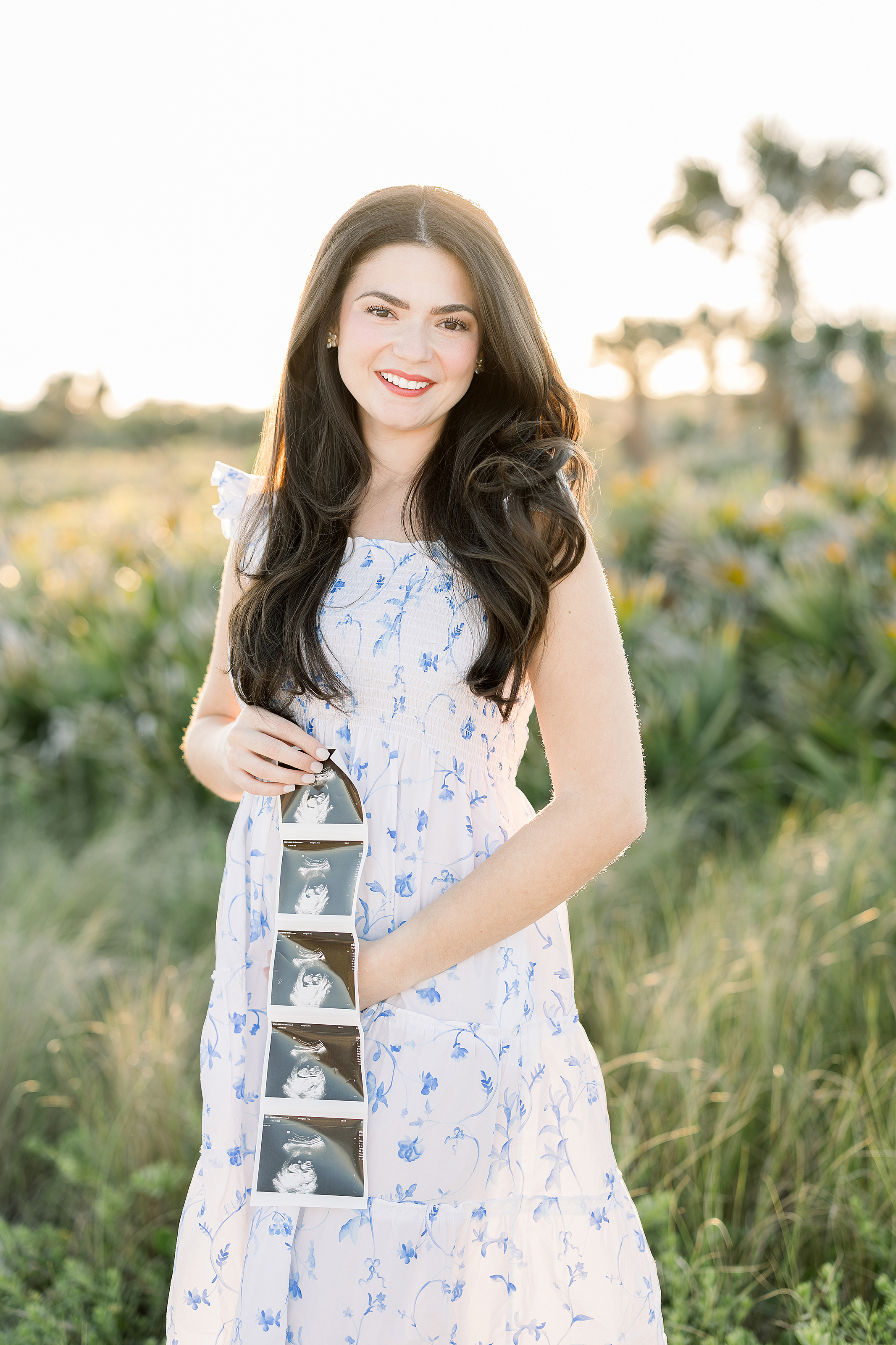 A Golden Hour sunset pregnancy announcement portrait of a woman in a blue and white dress.