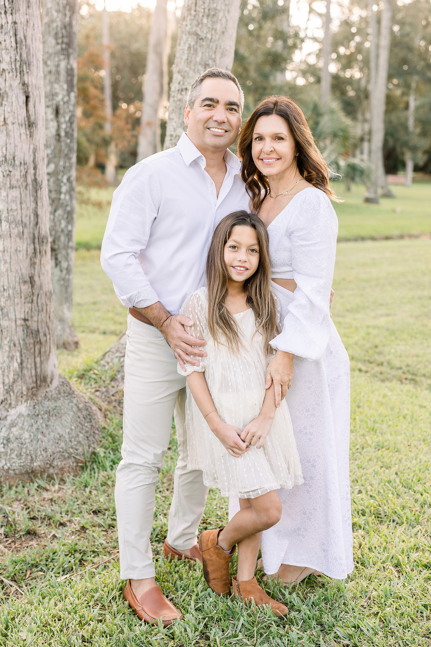 An airy portrait of a family of three dresses in white standing in Johansen Park.