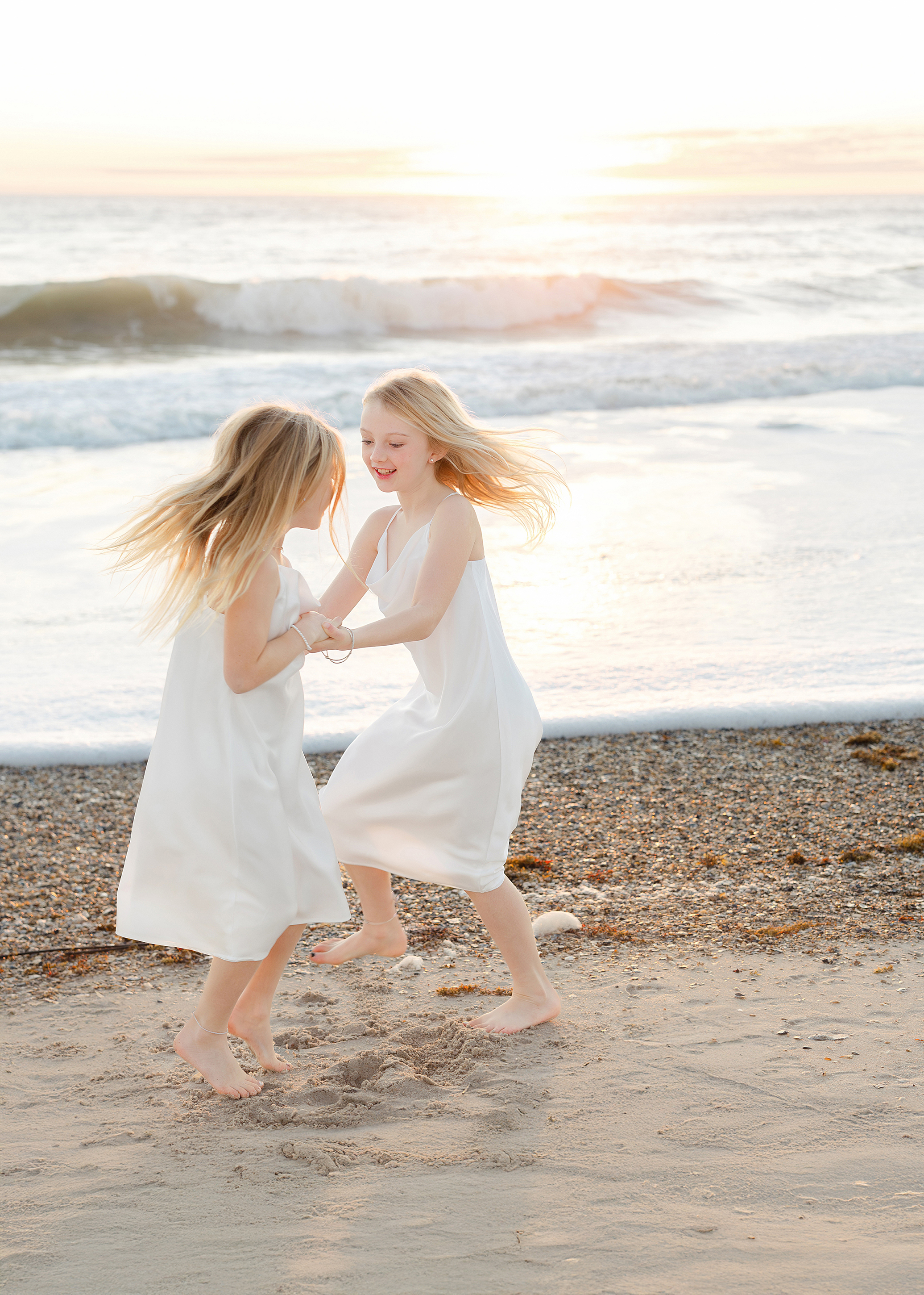 Two little girls in white dresses dance on the sand at the Omni Resort beach in Amelia Island, Florida.