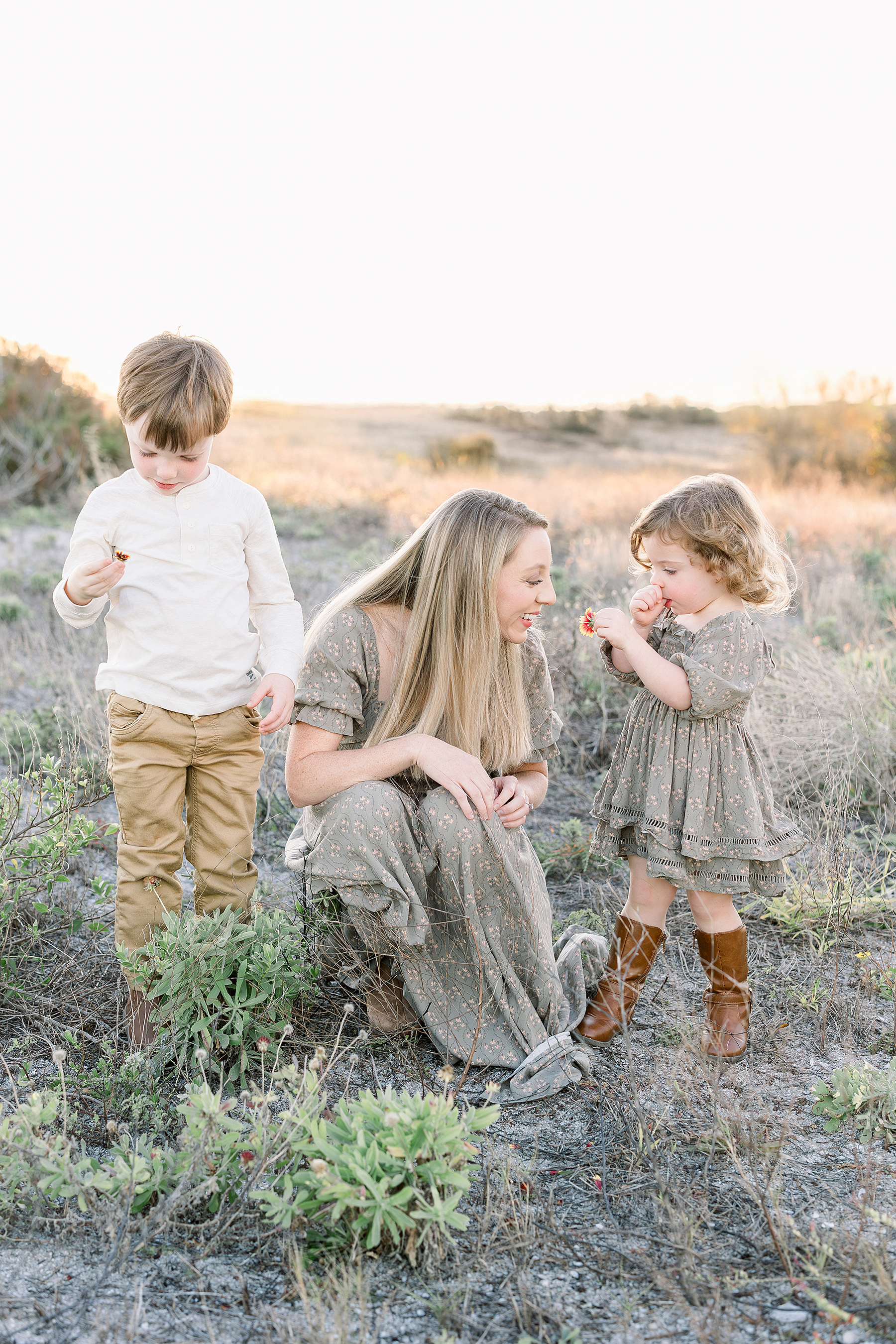 A mother kneels down with her two children wearing green dresses.