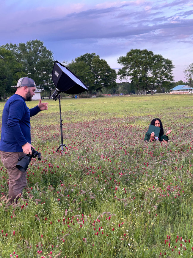 Photographer capturing a person sitting in a field of wildflowers with lighting equipment.