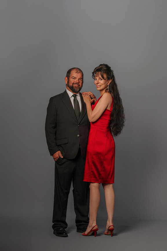 Man in a suit and woman in a red dress smiling against a gray background.