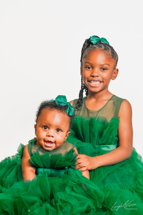 Two young girls in green dresses smiling and posing together for a cheerful photo.