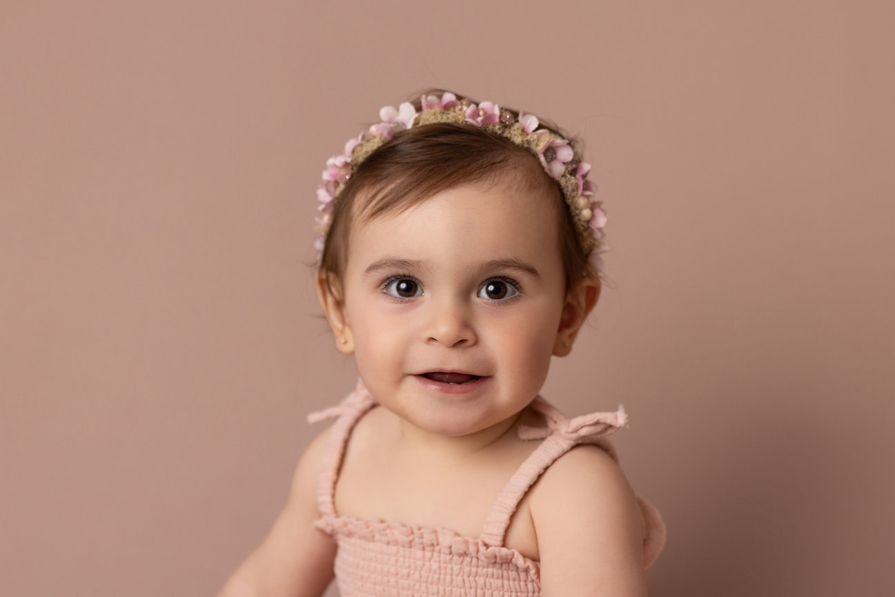 one year old portrait of a baby girl on a soft mauve backdrop