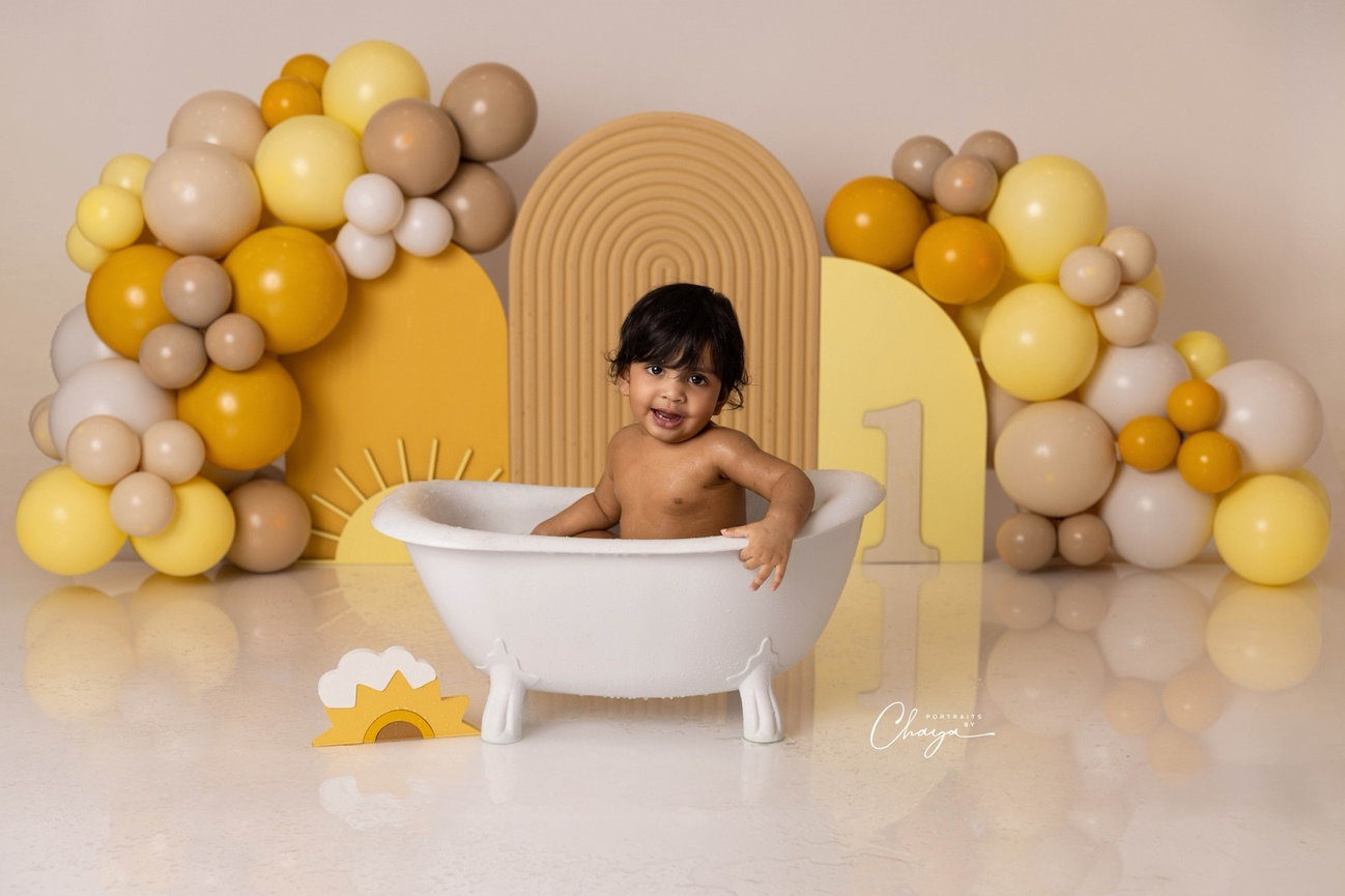 Baby smiling in a white tub during the milk-bath finale of a first birthday session