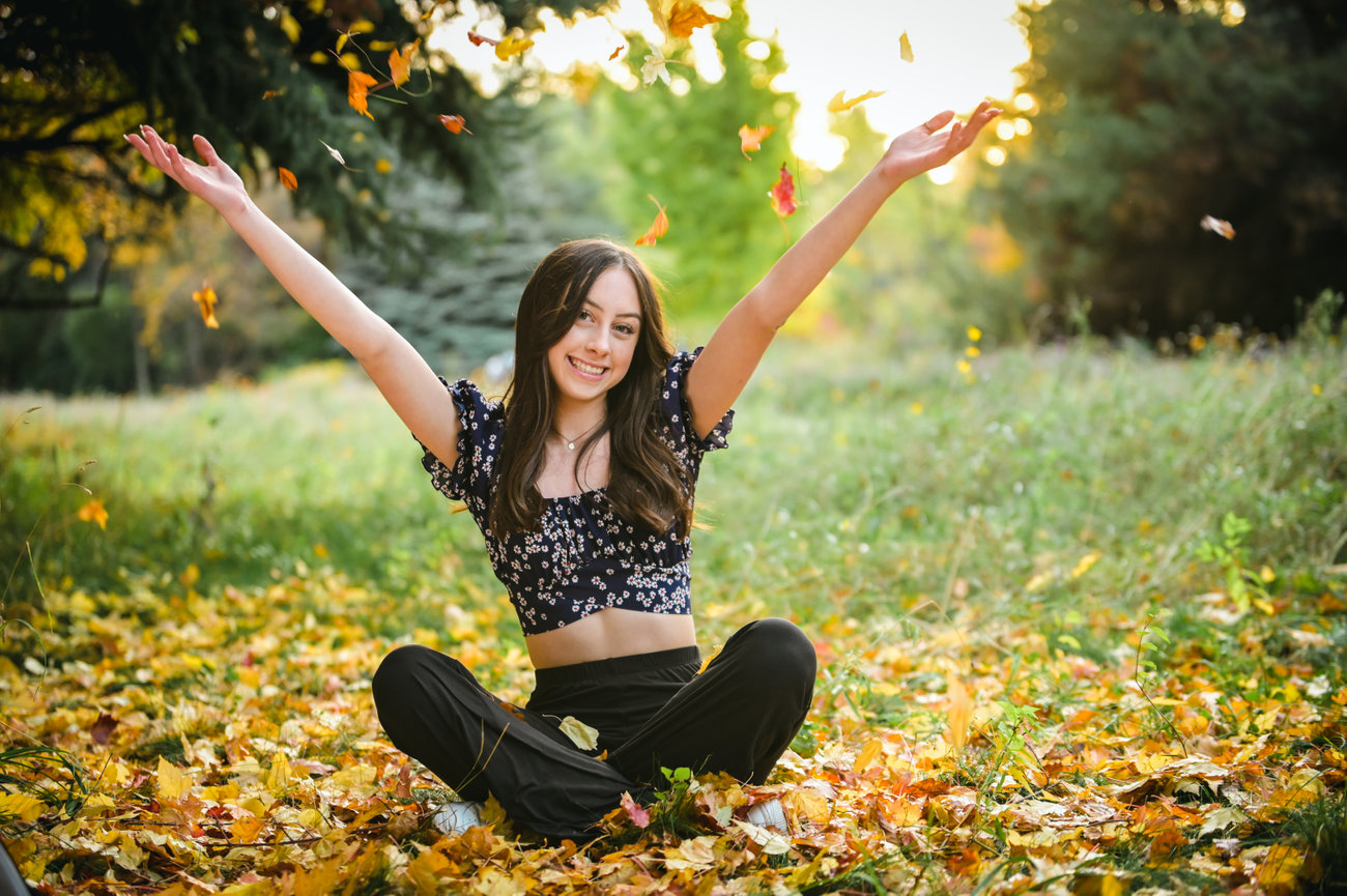 Senior year photo of a girl throwing fall leaves into the sky at a park in Boise, Idaho