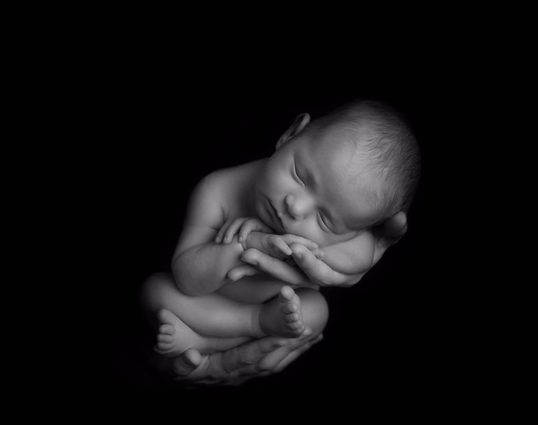 Newborn portrait of a baby relaxed in her mother's hands in delicate black and white.