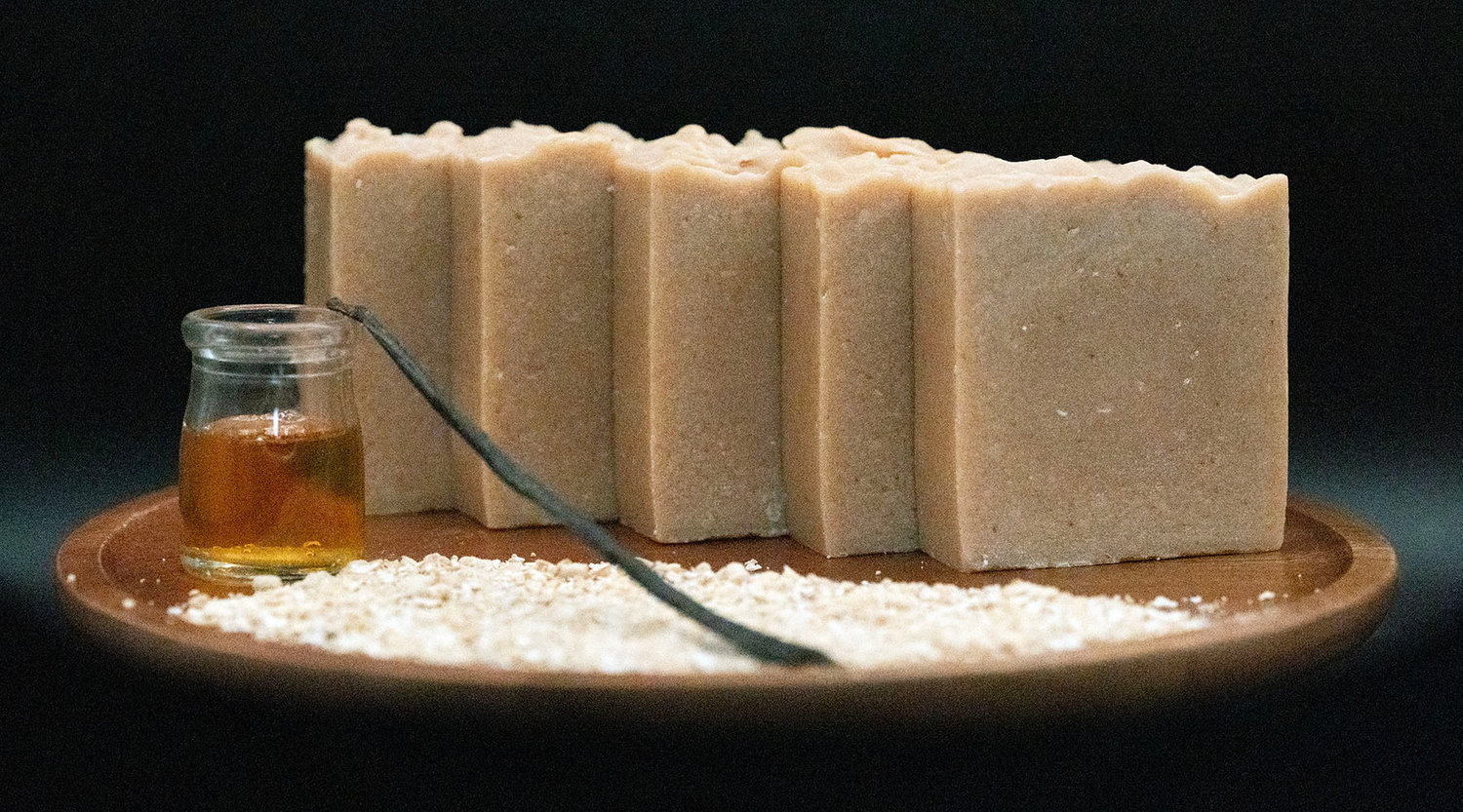Handmade soap bars on a wooden tray with a small bottle of amber liquid and white powder