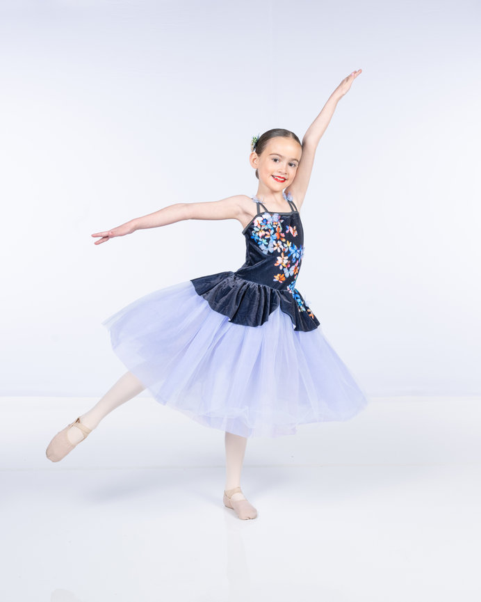 A young dancer in a tutu performs a ballet pose on a white background.