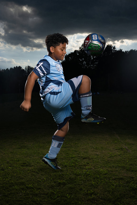 Young soccer player juggling a ball on a field under dramatic storm clouds