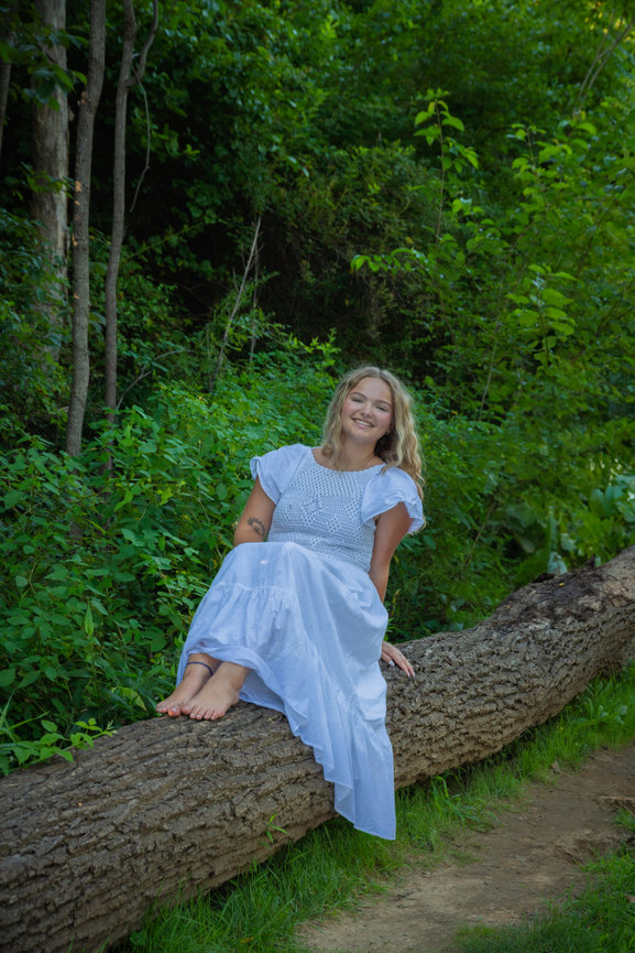 Woman in a blue dress sitting on a log in the forest