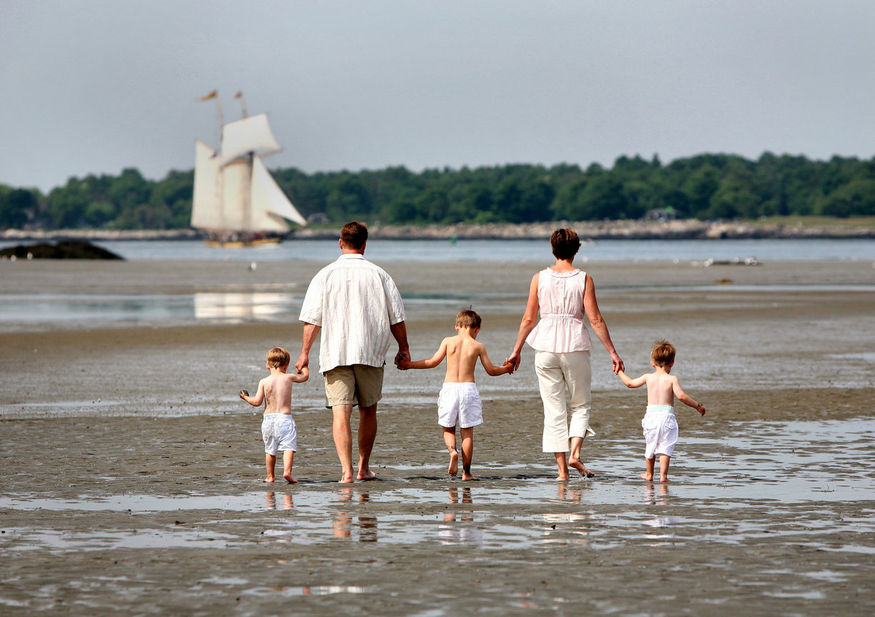 Family walking on a beach near a sailboat in the background