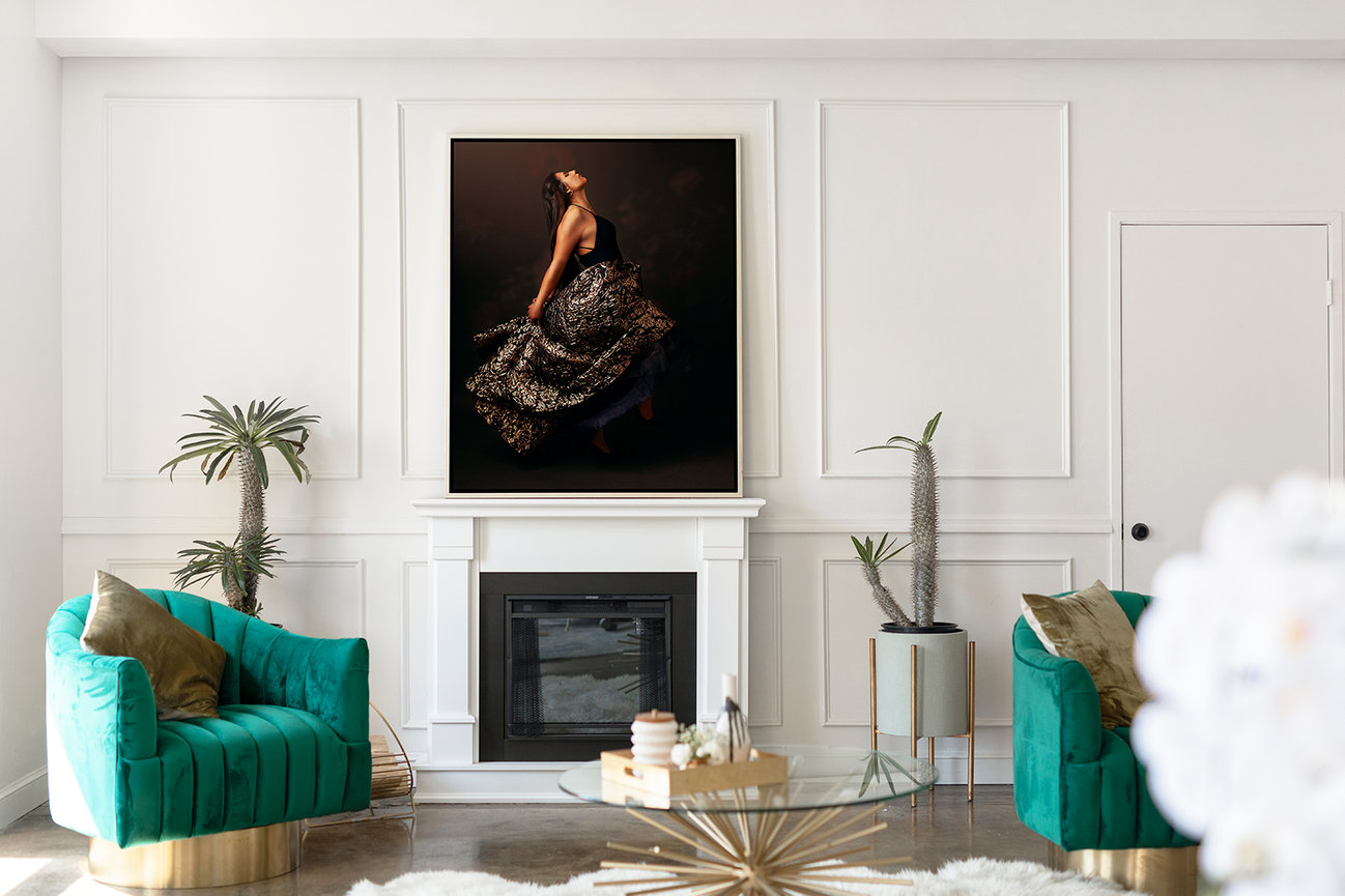 Luxurious living room with teal chairs, a glass coffee table, and a large portrait above a white fireplace mantel.