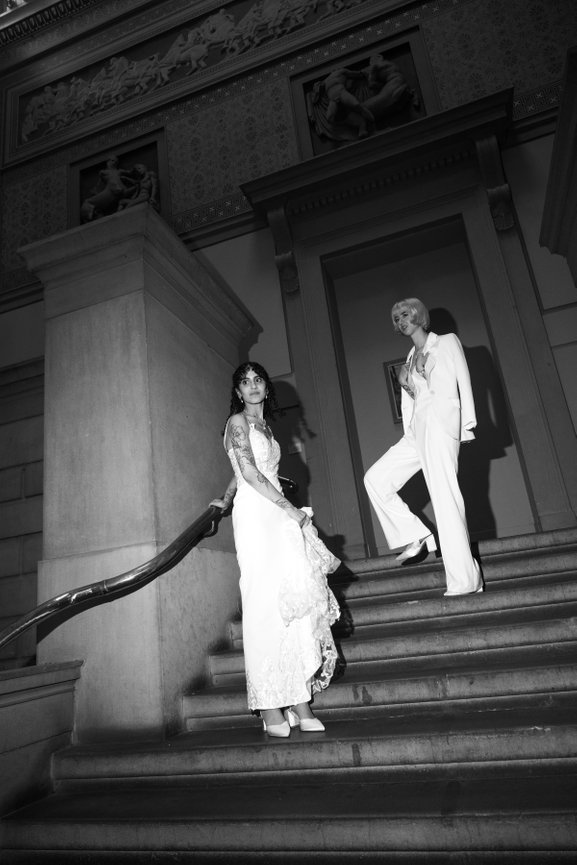 High contrast direct flash wedding photography of two brides on a historic staircase at Manchester Art Gallery, captured in bold black and white.