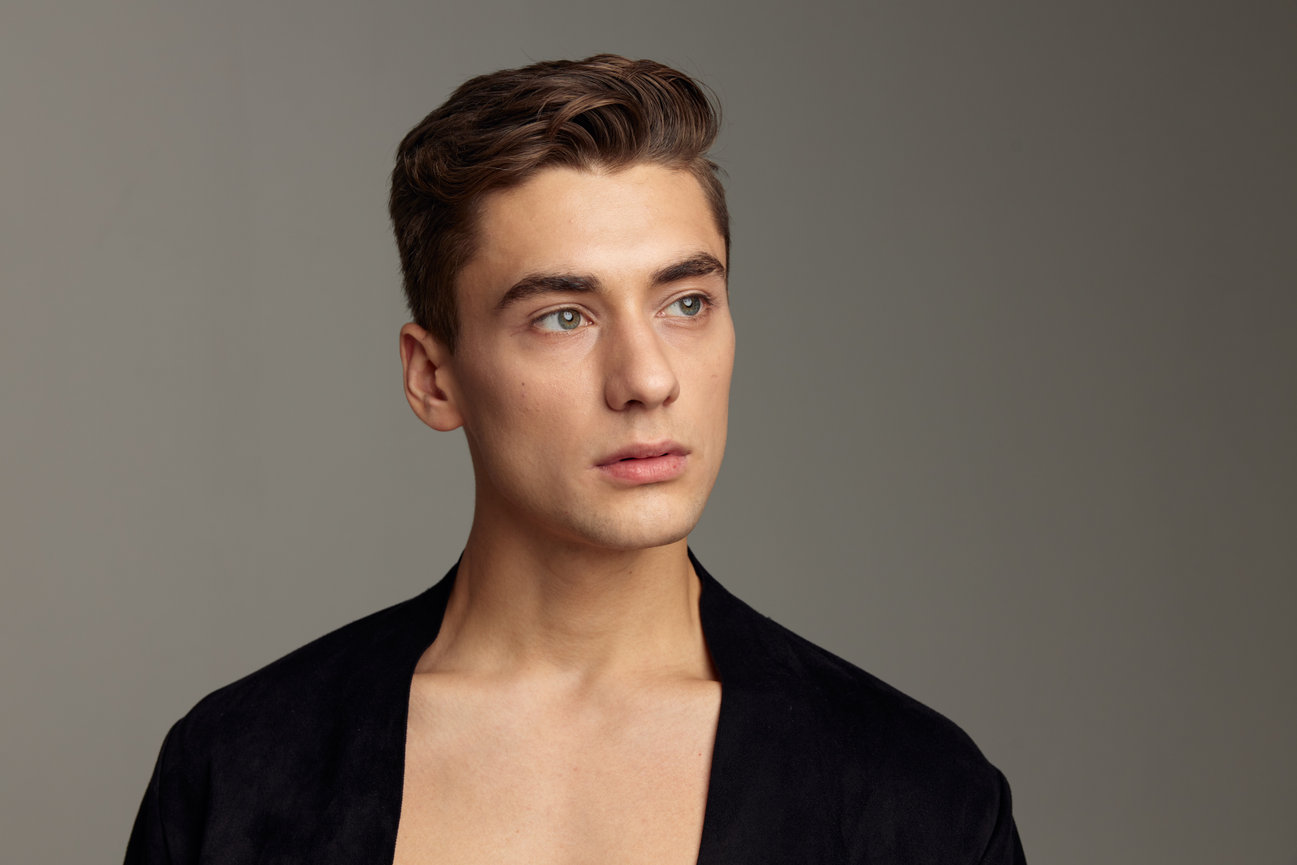 Studio portrait of a young man wearing a black jacket on a gray background.