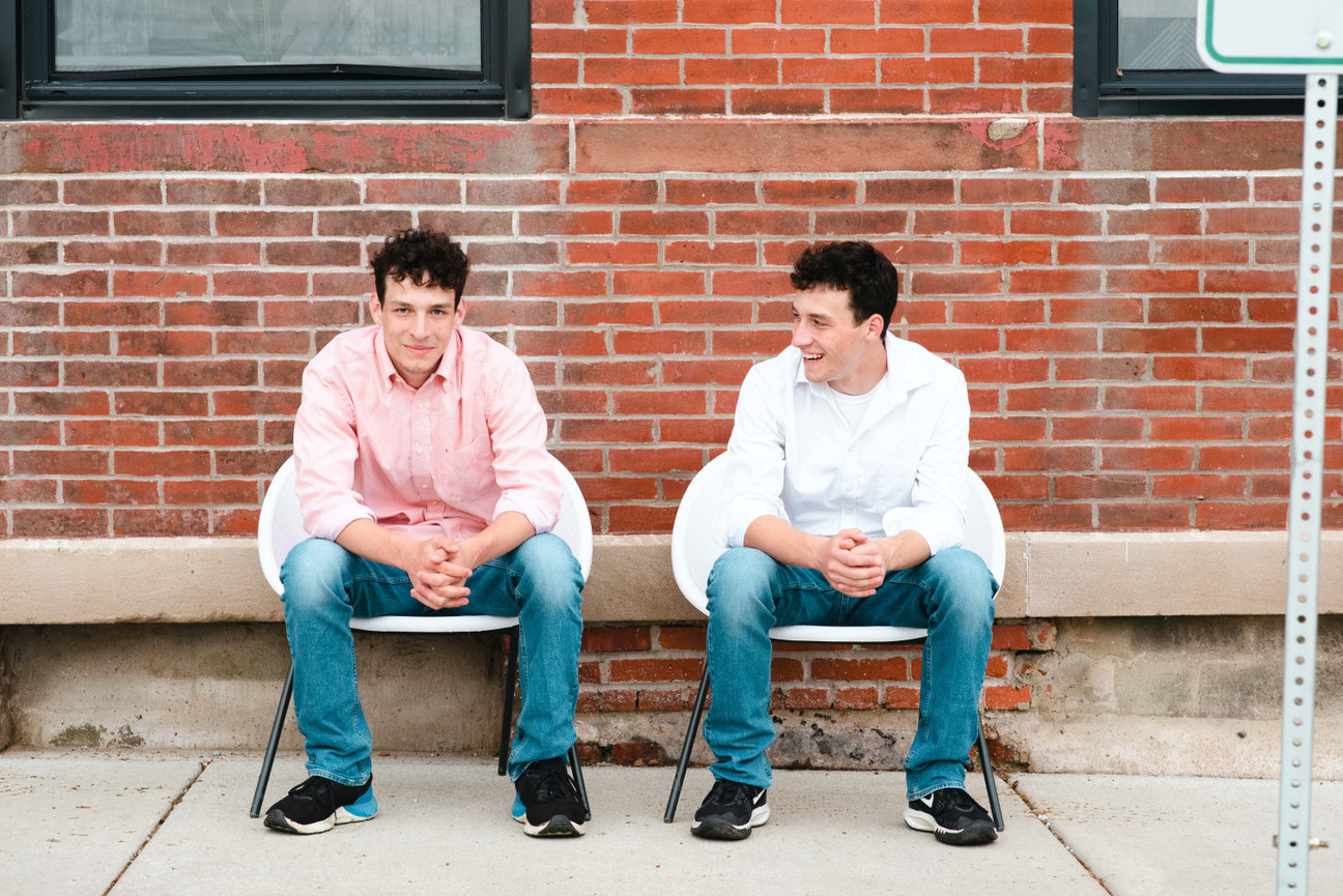 twin senior boys sitting in front of a brick wall