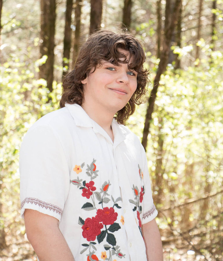 male high school senior outside with trees and sunlight in the background
