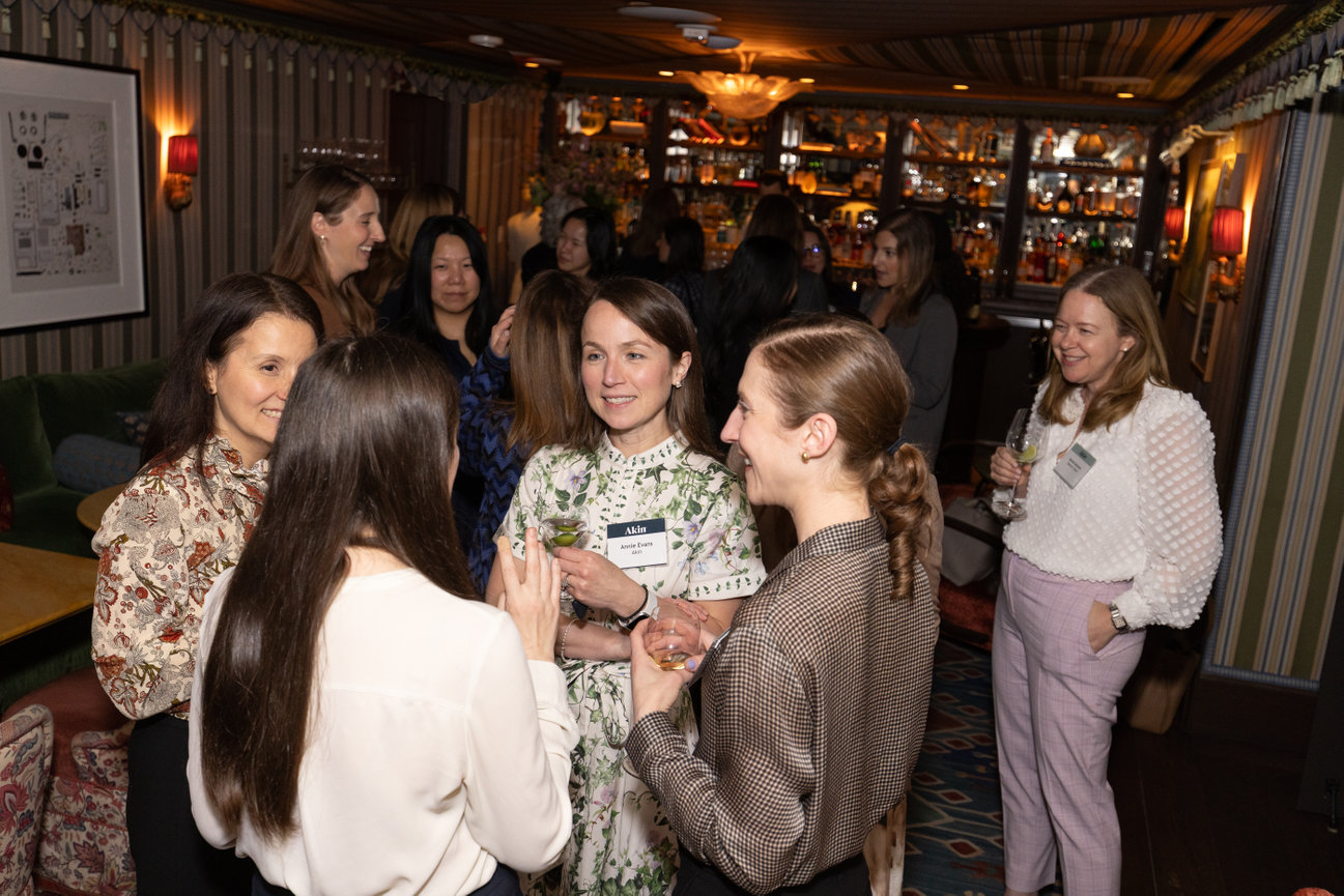 A group of women engaged in conversation at a social event in a stylishly decorated bar area.