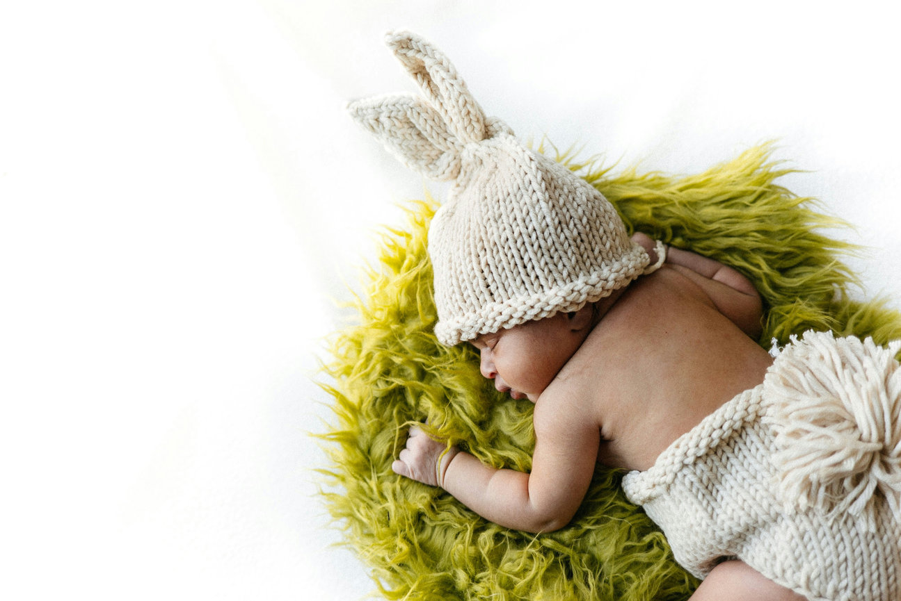 Sleeping newborn wearing a bunny hat on a yellow blanket
