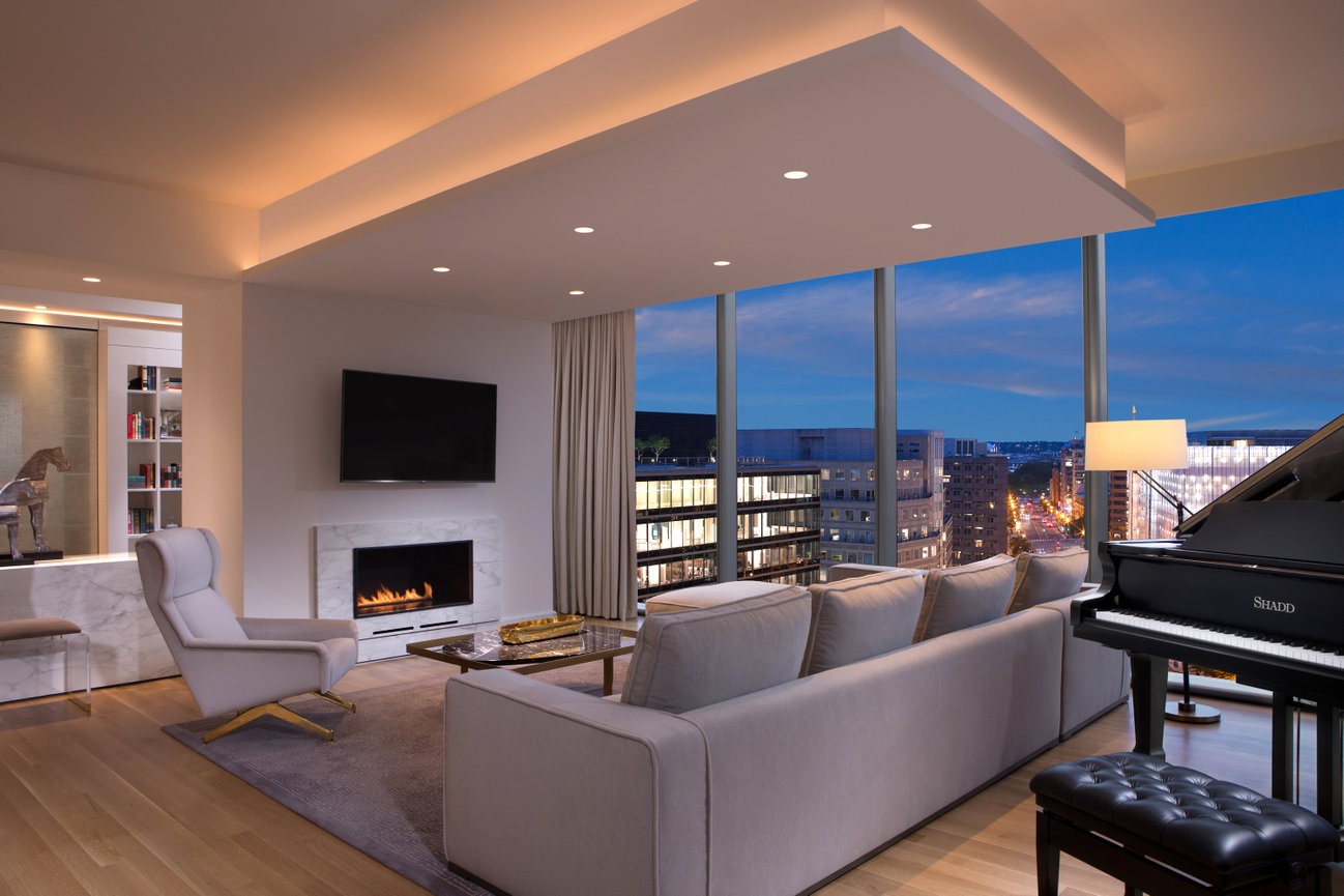 Presidential Suite at The Conrad Hotel in Washington DC showcasing the Living Room with Fireplace and piano with a view of the city.