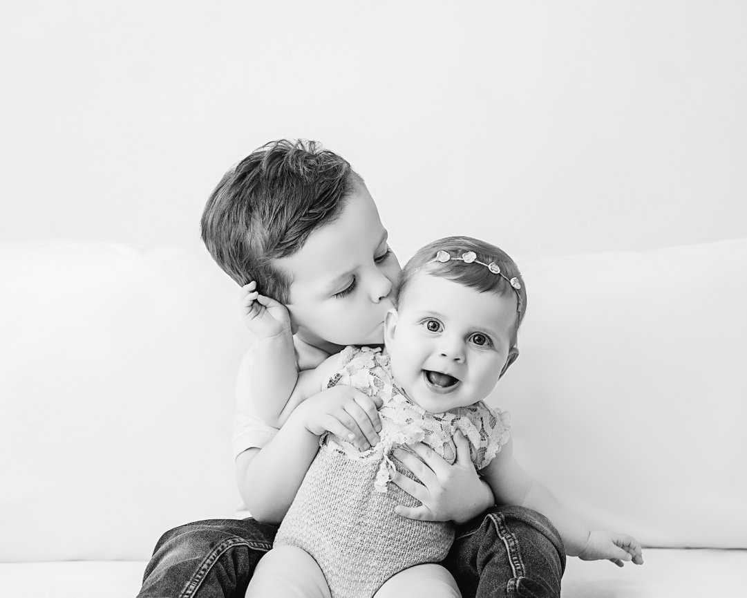 Older brother gently holding little sister on modern white couch