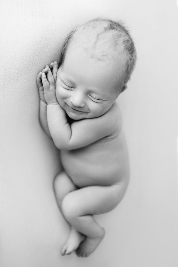 Fine art black and white newborn portrait on solid backdrop, highlighting baby's delicate features