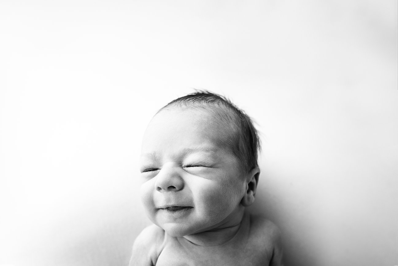 Black and white candid photo of one-week-old newborn making a funny face, capturing early personality and expression