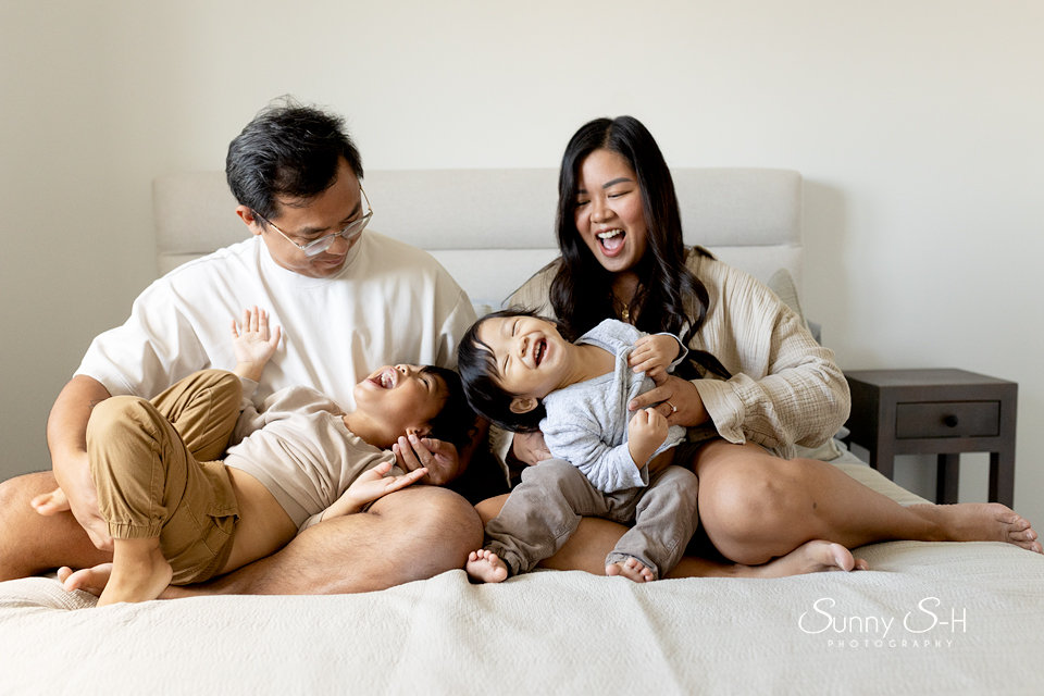 A joyful family sitting on a bed, laughing and playing together.