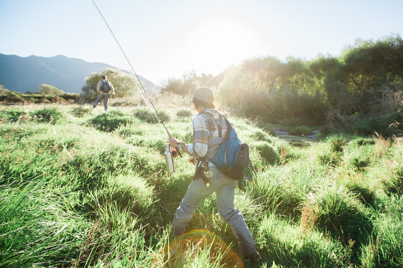 Person hiking through a sunny meadow with mountains behind