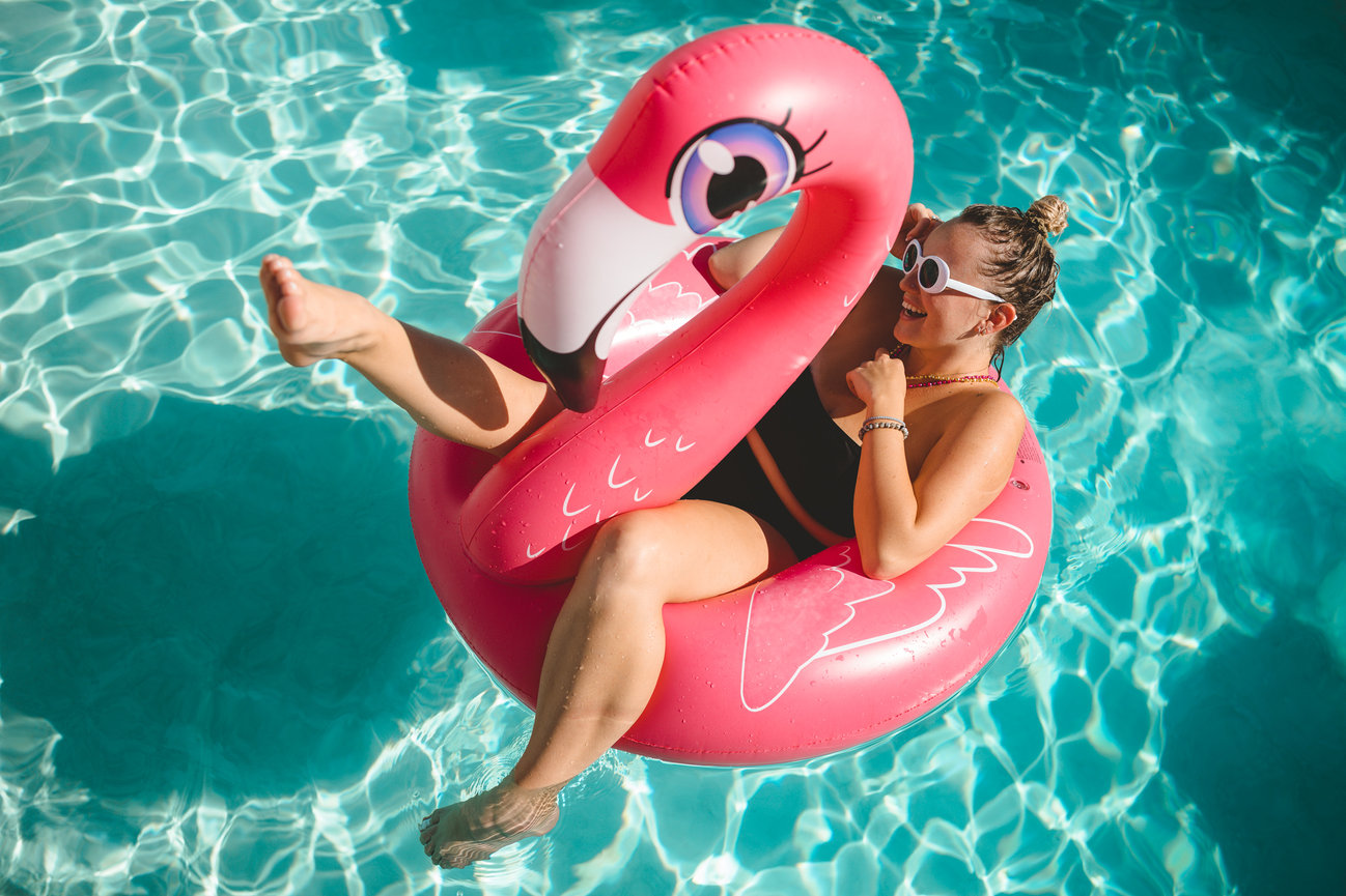 Woman floating on a flamingo pool float in clear blue water