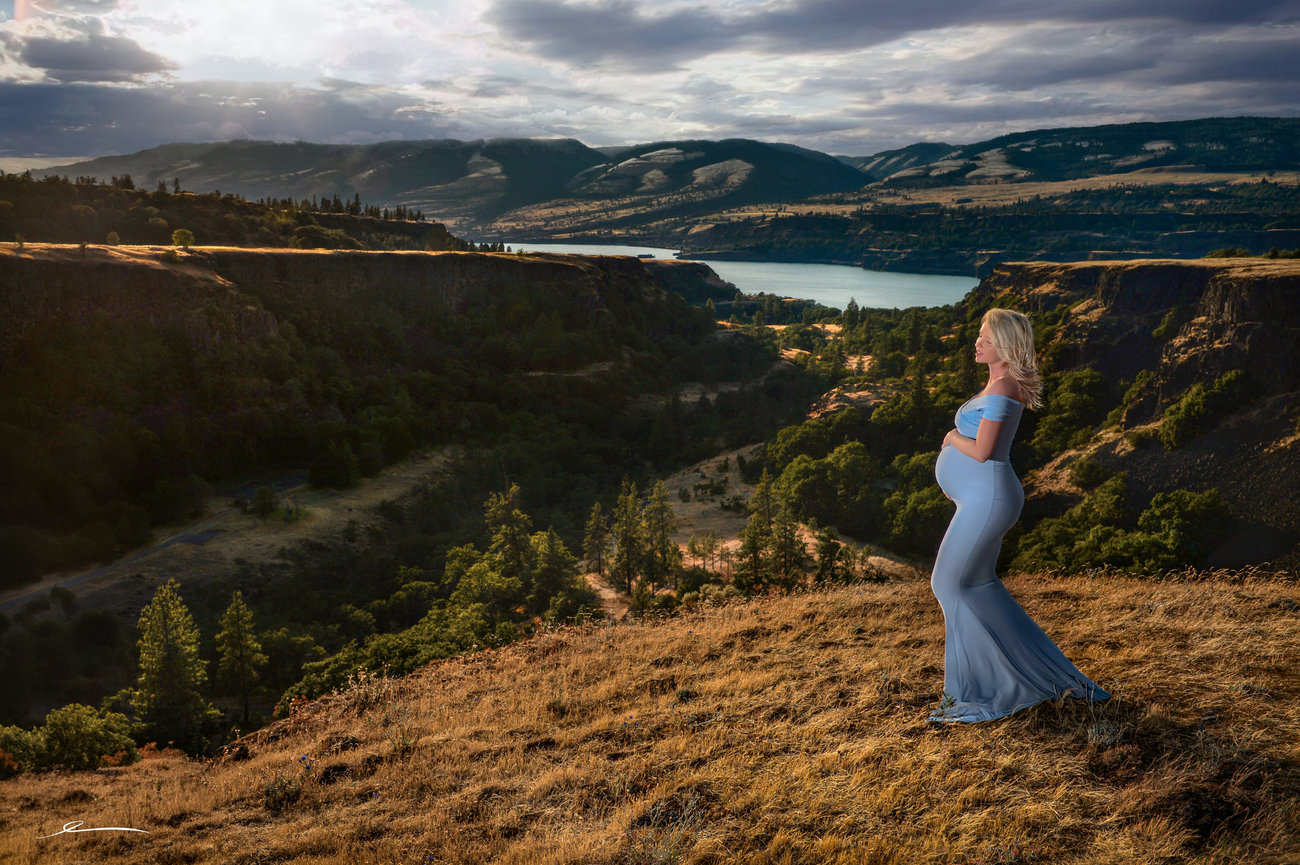 Woman standing on a hill overlooking a scenic valley at sunset.