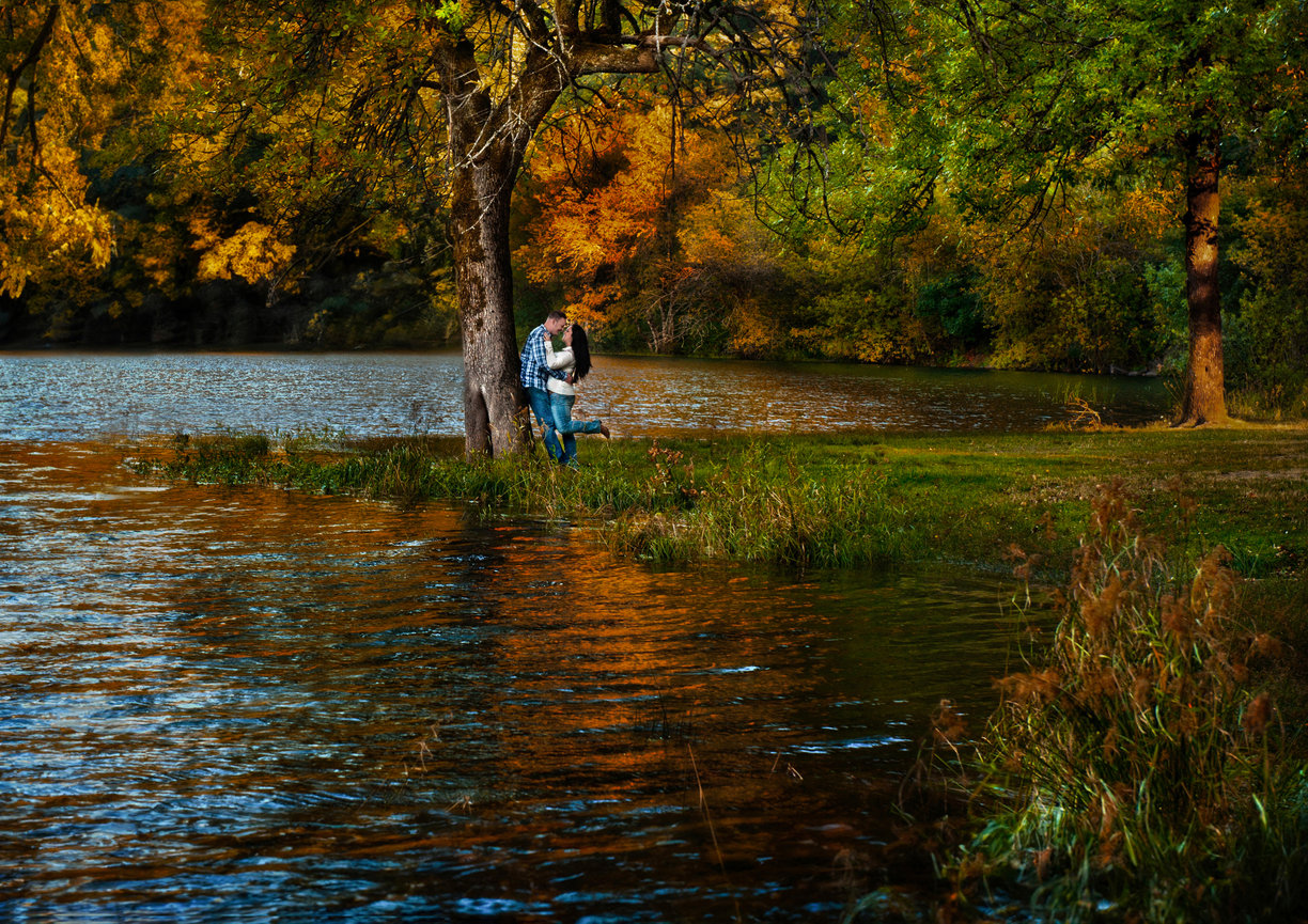 Person standing by a tree in shallow water during golden hour.