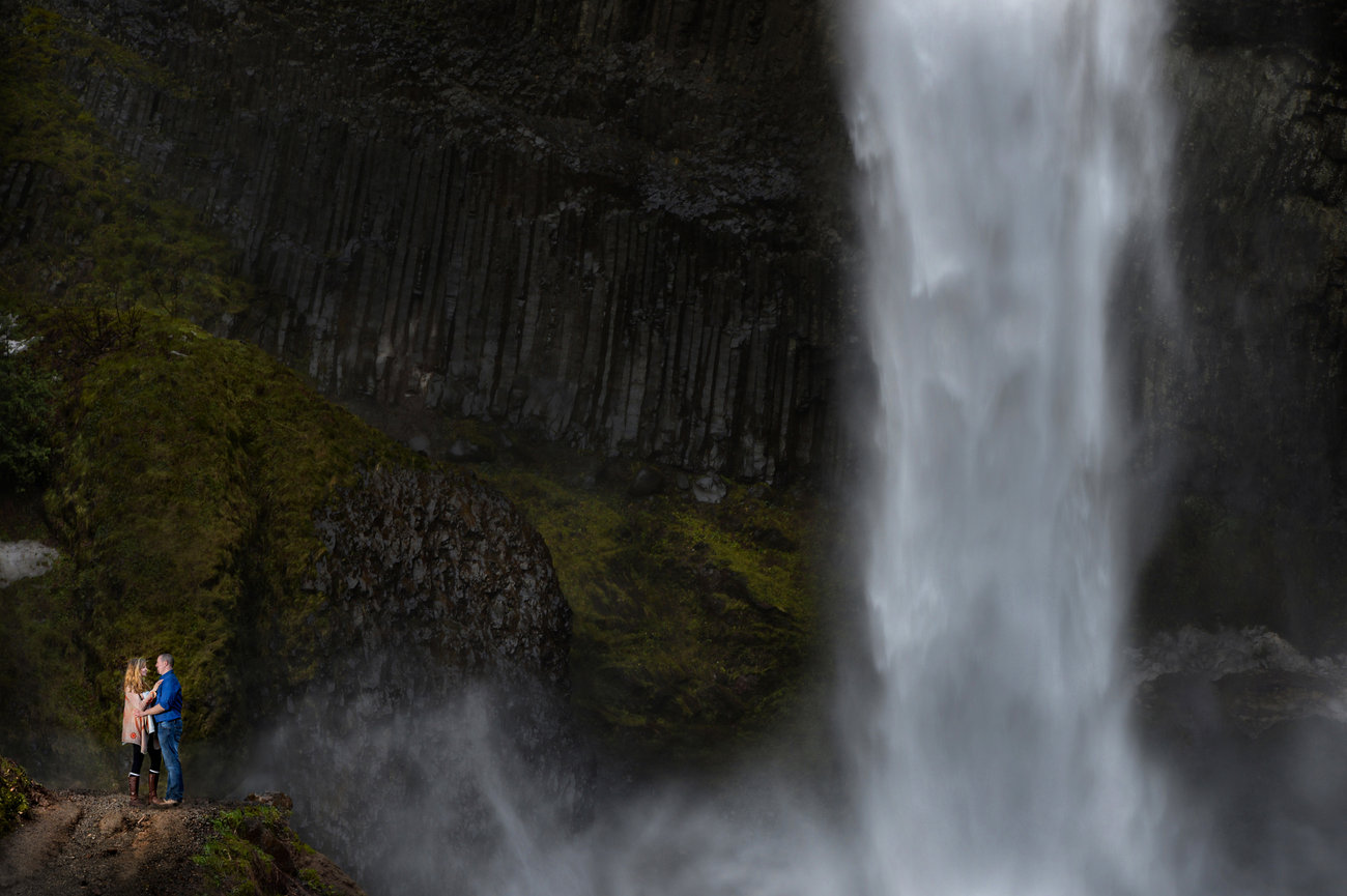 Person standing beside a powerful waterfall in a misty gorge.