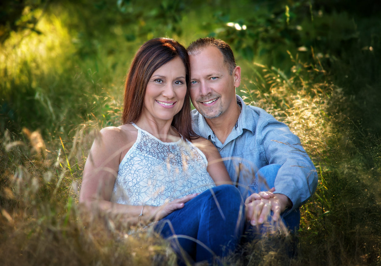 Couple sitting together in tall grass with sunlight behind them.