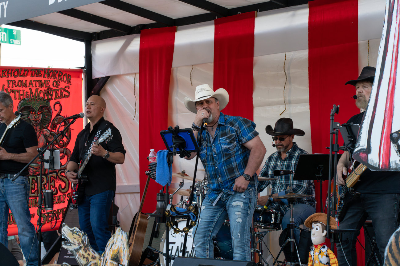 Live band performing on a outdoor stage with red and white backdrop.