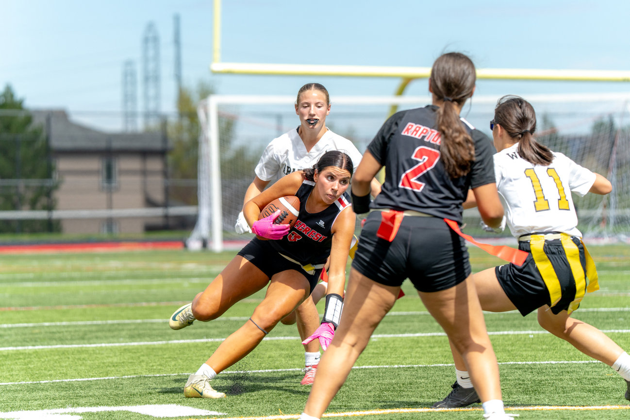 Girls playing flag football near the goalpost on a turf field.
