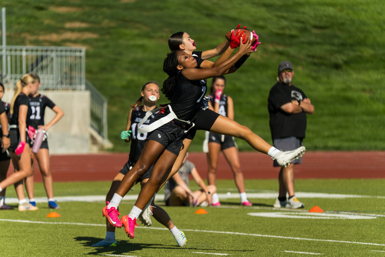 Two girls jump to catch a flag football pass on the field.