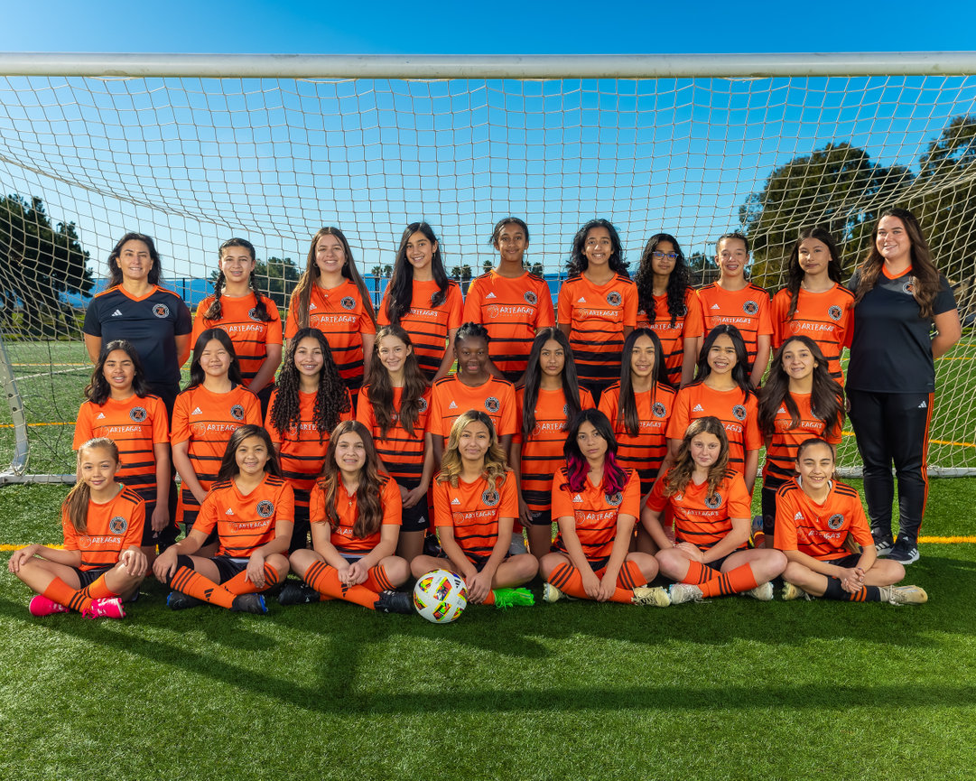 Girls soccer team posing in orange uniforms on the field.