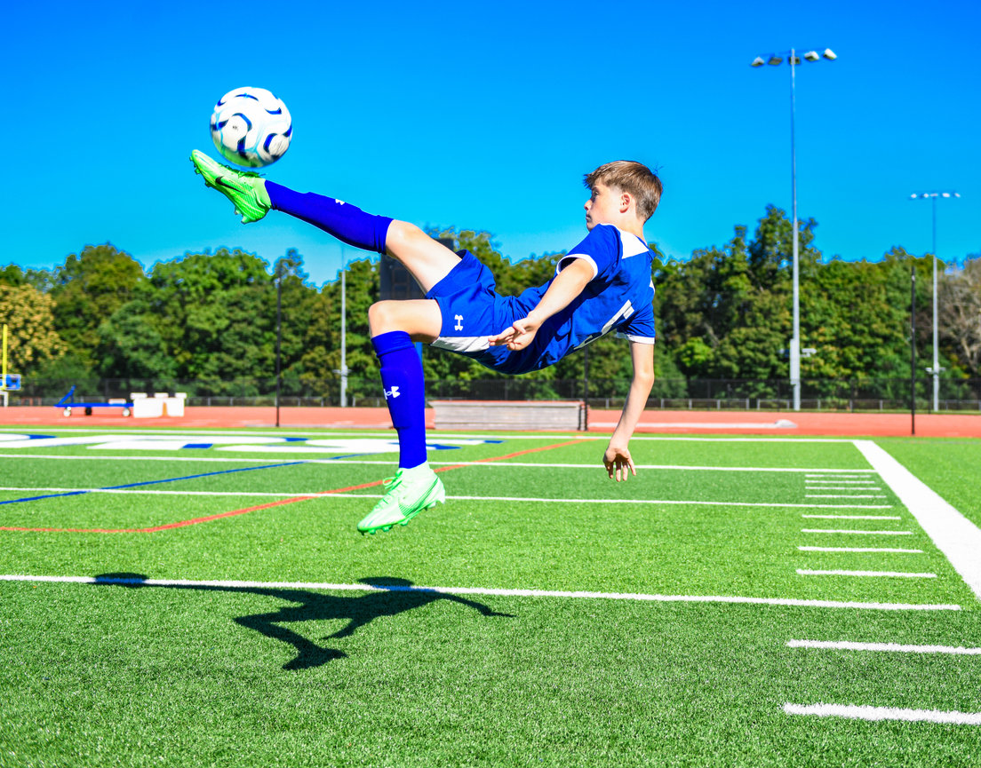 A soccer player leaps high to control the ball with one foot on a sunny field.