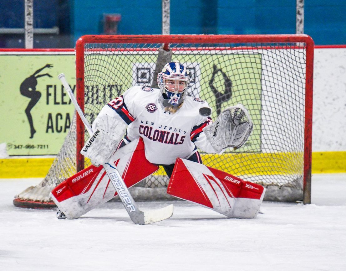 A hockey goalie crouches in front of the net and tracks the puck during play.