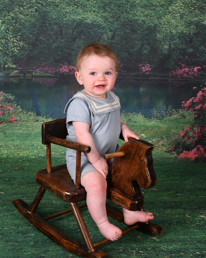 Smiling child on a wooden rocking horse by a garden pond