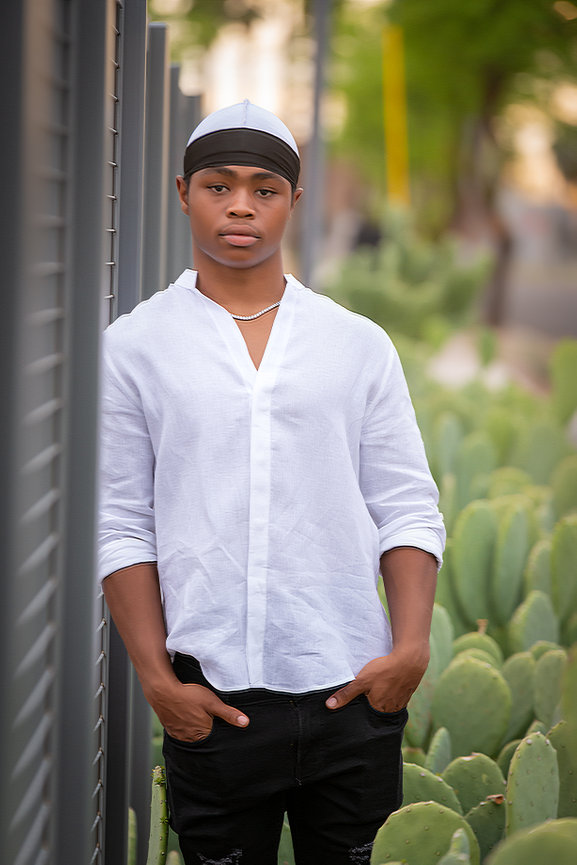 Senior boy in white shirt leaning against cactus wall