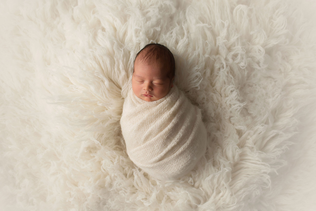 Newborn baby sleeping in cream knit wrap on cream fur at newborn photoshoot with Kansas City photographer Dreamworks Photography