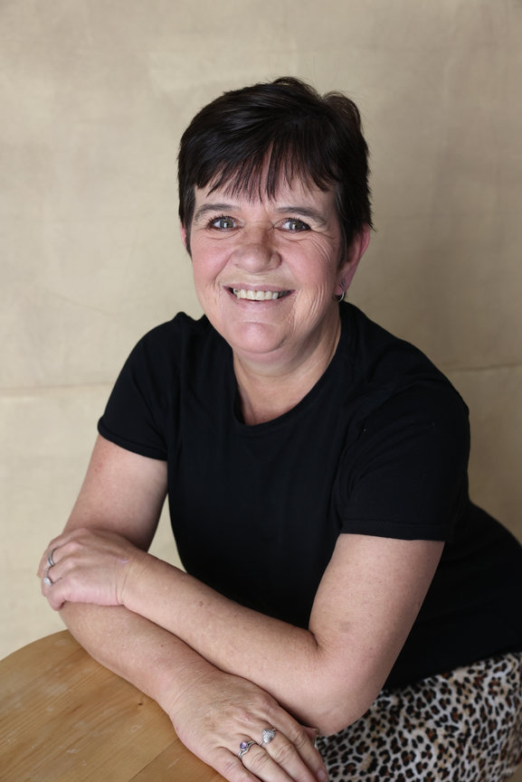 Smiling woman with short dark hair leaning on a table against a beige background. melbourne website photographer