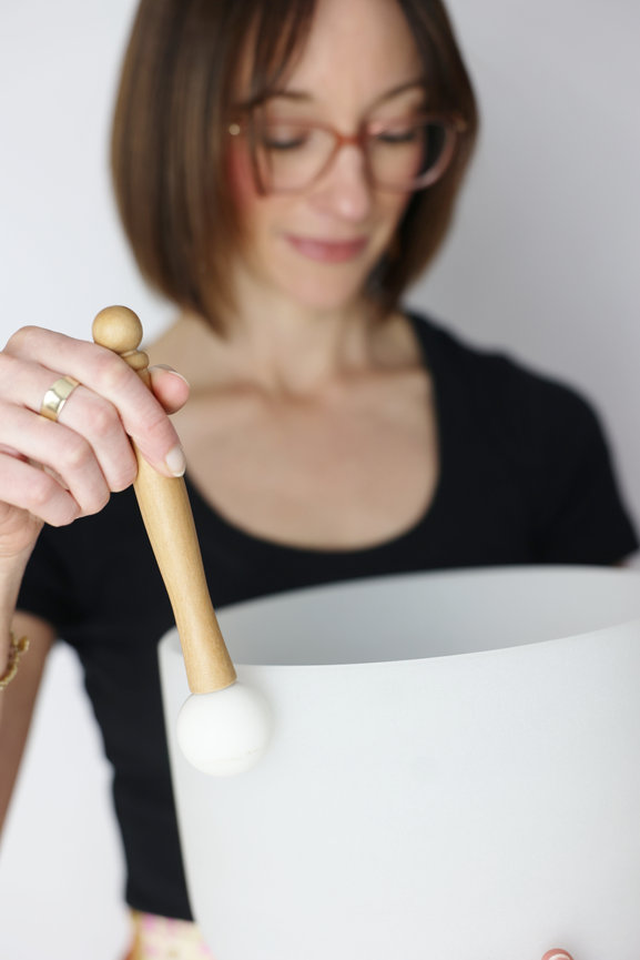 Woman holding a wooden singing bowl mallet over a white bowl. melbourne website photographer