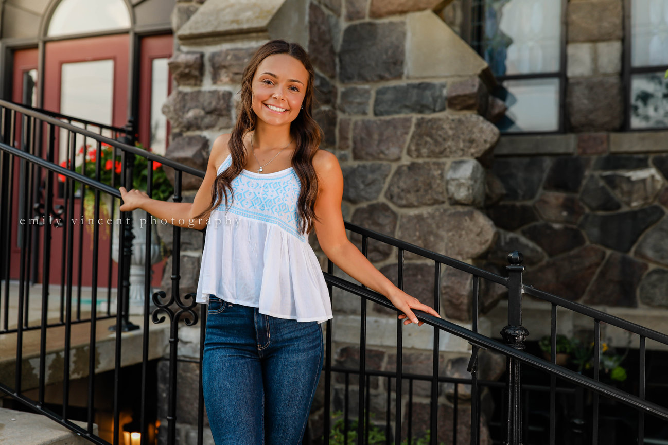 High school senior girl against railing, smiling outdoors during a Farmington senior photography session