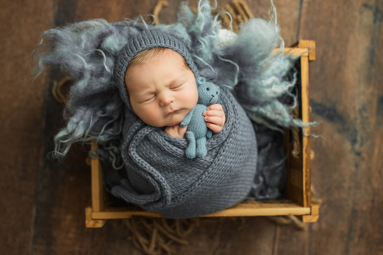Newborn baby swaddled in knitted blanket holding tiny bear