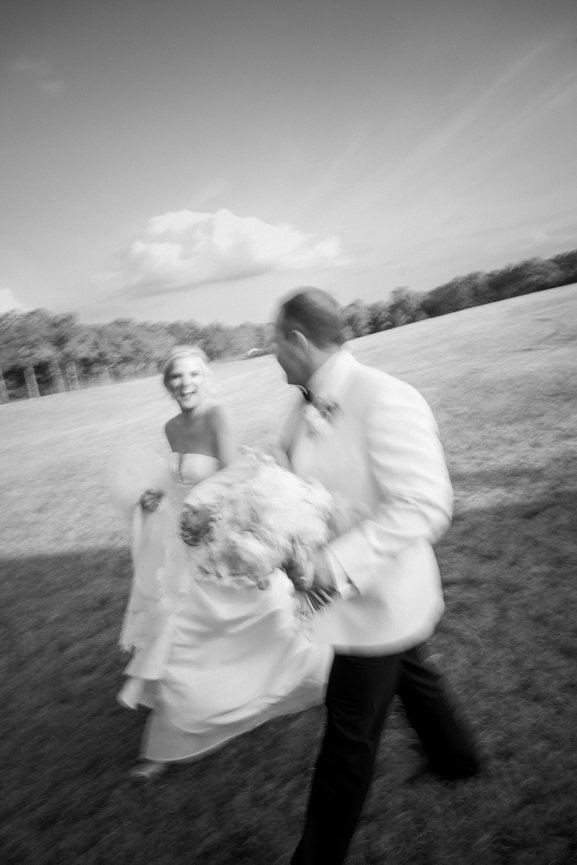 Black and white motion blur photo of bride and groom laughing and walking in a field. Wedding photography by Heather Durham.